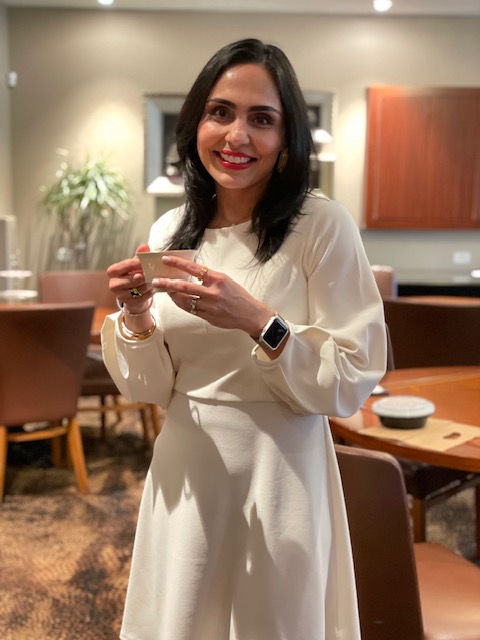Dr. Naureen Alim smiling, holding a cup of tea in a lounge.